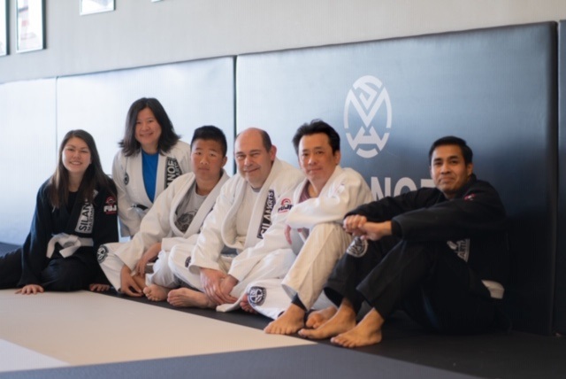 The students of the Saturday morning BJJ All Levels class lined up against the mat wall at Silanoe 