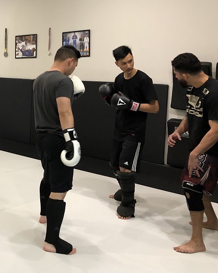 Wah Wu is being shown by Coach Luis how to execute a leg kick with proper technique. His training partner Ken is also in the Muay Thai Kickboxing class.