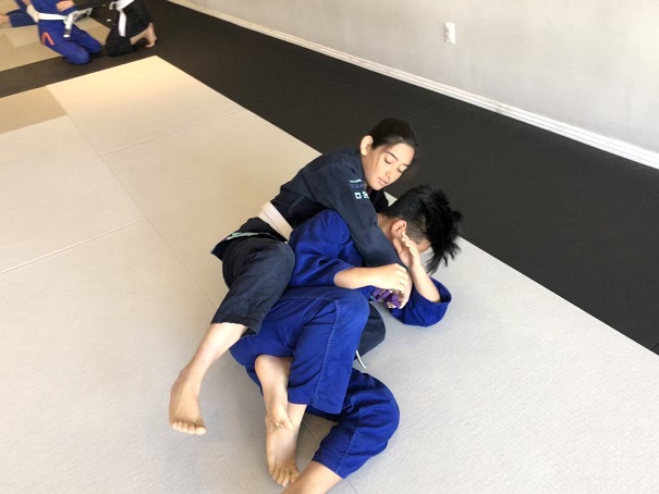 Ally M. securing the hooks after getting the seatbelt grip on her training partner Ethan P. at the Teens Adults All Levels at Silanoe in San Gabriel.