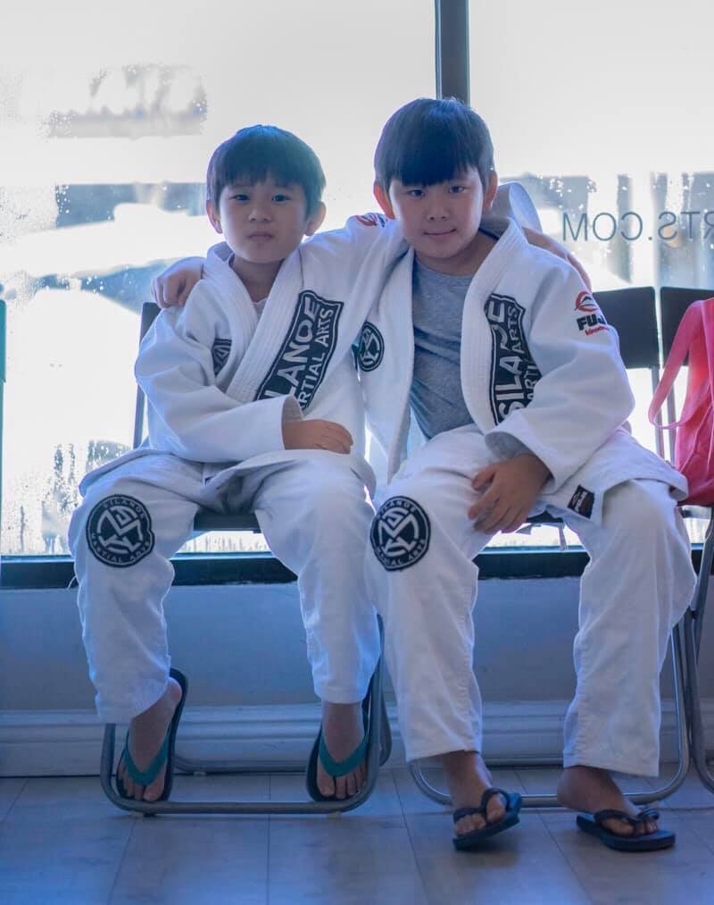 Brothers Alex and Charles on a chair resting after training hard together at the Saturday morning Kids Jiu-Jitsu class