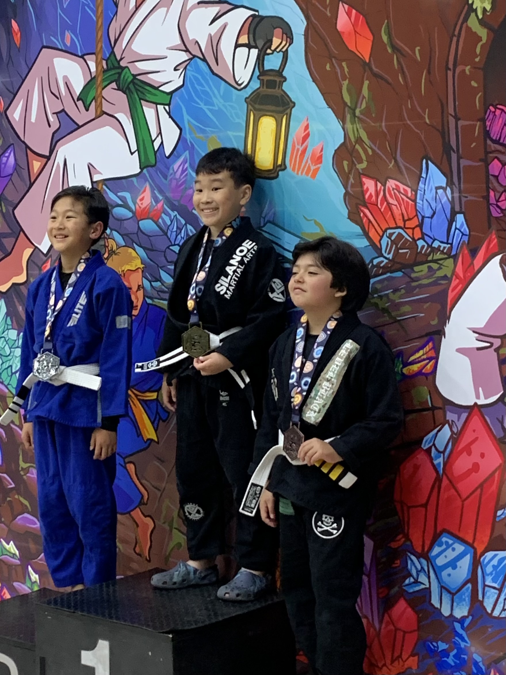 Silanoe Martial Arts Kids competitor Lucas L. taking gold at Dream BJJ competition Kids BJJ competitor of Silanoe Martial Arts San Gabriel Lucas L. standing on the podium after taking gold at Dream BJJ competition
